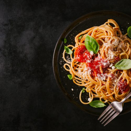 Tasty appetizing classic italian spaghetti pasta with tomato sauce, cheese parmesan and basil on plate on dark table. View from above, horizontal