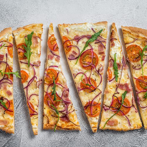 French tarte flambee with cream cheese, bacon, tomato and onions. Flammkuchen from Alsace region. White background. Top view.