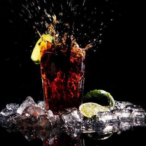 Fresh cola drink with splashes of water and green lime on black background