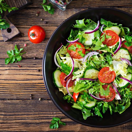 Salad from tomatoes, cucumber, red onions and lettuce leaves. Healthy summer vitamin menu. Vegan vegetable food. Vegetarian dinner table. Top view. Flat lay